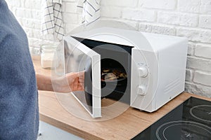 Woman opening modern microwave oven in kitchen