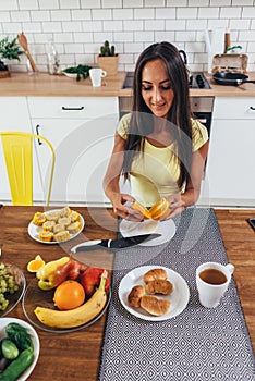Woman at kitchen table having dinner, eating orange.