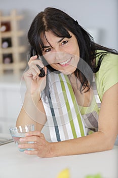 Woman in kitchen on telephone holding glass water