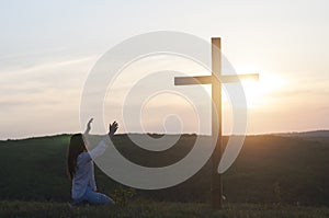 A woman is kneeling with her hands up. Near the cross. Prayer of repentance. Christian faith.