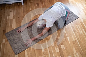 woman kneeling on a mat and doing a balasana asana while practicing yoga at home