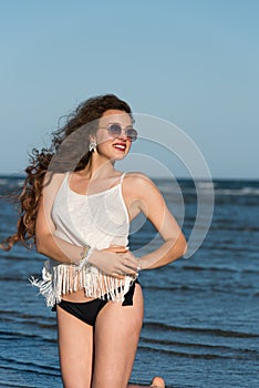 Woman kneeling in sea water wear bikini, sunglasses and white shirt
