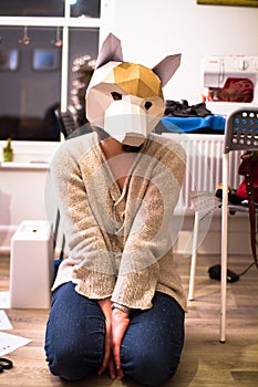 A woman kneels on the ground wearing a fox mask