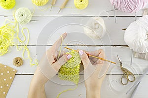 Woman knits clothes. Top view white desk with tools and knitting accessories. Women`s hands hold knitting needles