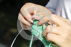 Woman knits clothes from wool with knitting needles.