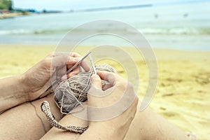 Woman knits grey yarn openwork pattern with metal knittings on beach