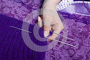 A woman knits knitting, lying in bed. A product made of string of purple.