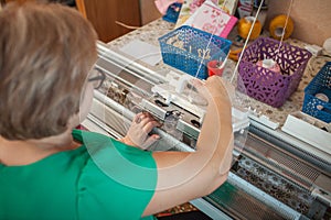 A woman knits on a knitting machine,