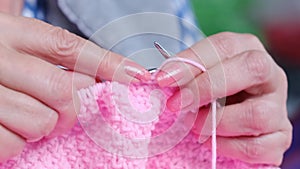 woman knits on knitting needles with pink threads