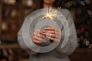 Woman in knitted sweater celebrates the holiday with amazing sparklers in female hands. Close-up.