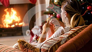 Woman knitting in armchair next to burning fireplac eand glowing Christmas tree