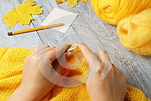 Woman knitting a warm wool sweater on knitting needles with yellow yarn