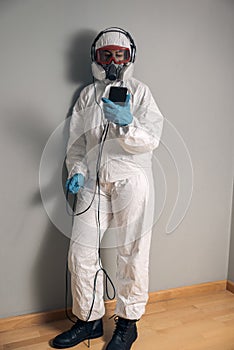 Woman in lab coat, nitrile gloves, goggles, face mask and NBC protective suit, smartphone mobile phone in hand, with music