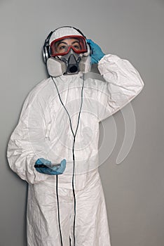 Woman with lab coat, nitrile gloves, safety glasses, face mask and NBC protection suit, with the mobile phone smartphone in hand,