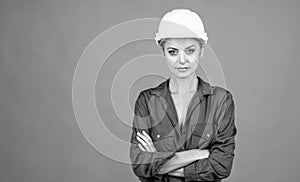 woman laborer in protective helmet and boilersuit on orange background, copy space, building