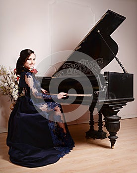 Woman in lace deep blue dress playing the piano and flowers. Retro vintage style