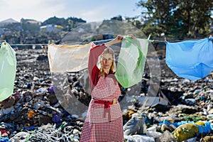 Woman on landfill hanging plastic bags as laundry. Consumerism versus plastic pollution concept.