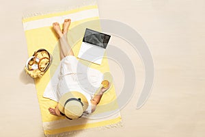 Woman with laptop, bag and headphones drinking juice sitting on the beach towel and enjoying summer vacation. Top view. Copy space