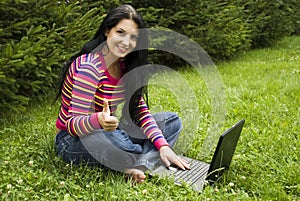 Woman with laptop in nature give thumbs up