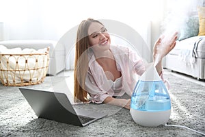 Woman with laptop near modern air humidifier at home