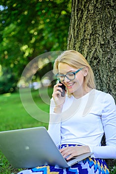 Woman with laptop in park order item on phone. Girl takes advantage of online freelance job. Girl sit grass with
