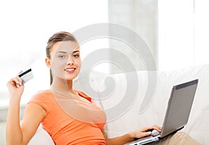 Woman with laptop showing credit card at home