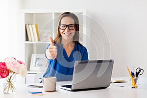 Woman with laptop showing thumbs up at office