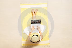 Woman with laptop sitting on the beach towel and enjoying summer vacation. Top view.