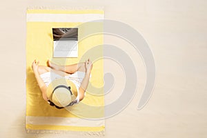 Woman with laptop sitting on the beach towel and enjoying summer vacation. Top view. Copy space.