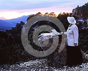 Woman with laptop standing on mountaintop at sunset