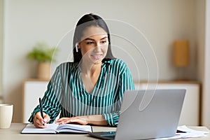 Woman At Laptop Taking Notes Learning Wearing Earbuds In Office