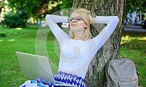 Woman with laptop works outdoor, park background. Taking advantages of free wi fi. Girl sit grass lean tree trunk with