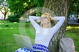 Woman with laptop works outdoor, park background. Taking advantages of freelance. Girl sit grass lean tree trunk with