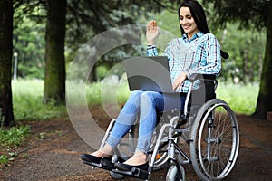 Woman with laptop works in wheelchair in park