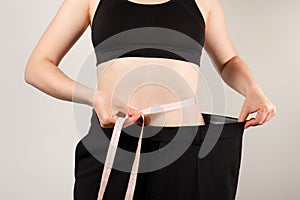 A woman in large pants measures the circumference of the abdomen, the concept of losing weight and a healthy lifestyle