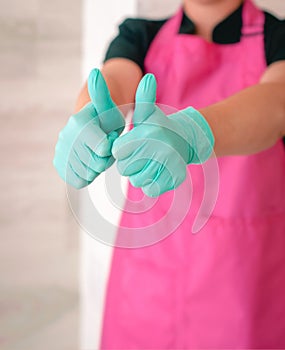 Woman in latex gloves and pink apron holding thumbs up as a hope symbol.