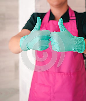 Woman in latex gloves and pink apron holding thumbs up as a hope symbol.