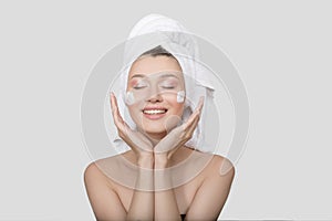 Woman is laughing with cream on her face and a towel on her head. White background. Skin care concept