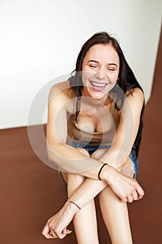Woman laughing with eyes closed, sitting on white and brown background