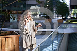 Woman laughs during phone call. Businesswoman talking on her telephone, standing in beige suit outside business center
