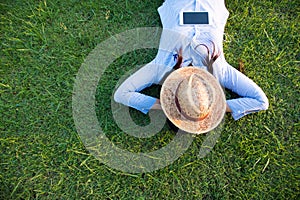 Woman lay down sleep on green grass meadow garden summer sunshine day happy time outside. Hipster Freelance work on laptop use hat