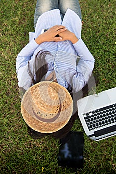 Woman lay down sleep on green grass meadow garden summer sunshine day happy time outside. Hipster Freelance work on laptop use hat