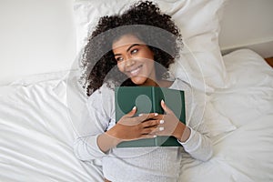 Woman Laying in Bed Holding a Book, Looking Away