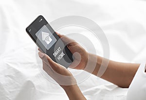 Woman laying in bed, using smart home app on smartphone