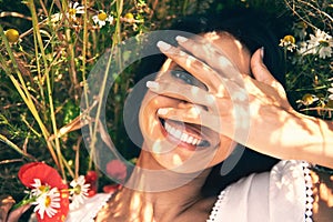 Woman, laying and closeup in field, smile or peek for portrait in spring, vacation or sunshine in nature. Girl, happy