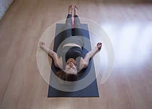 Woman laying on gray mat in relaxing pose on the floor, yoga class, front view