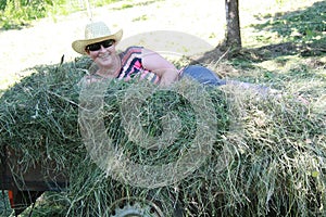 Woman laying in the hay. Putting the grass on the trailor. Farm chores, working on a field.