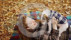 Woman laying on a plaid with her jack russell terrier puppy in autumn park and having fun