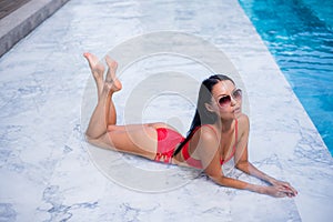 woman laying and relaxed near pool at cool black fashionable sunglasses,bra bikini pans, tan glowing skin woman