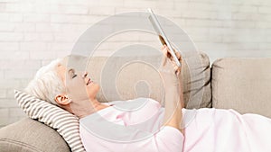 Woman Laying on Top of a Couch Holding a Tablet